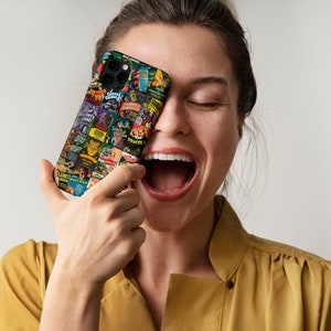 Puede incluir: Una mujer se r&iacute;e mientras sostiene una funda negra para iPhone con un collage de carteles de pel&iacute;culas de terror vintage. Los carteles presentan t&iacute;tulos como "Frankenstein", "Dr&aacute;cula", "La Criatura de la Laguna Negra" y "El Hombre Lobo".