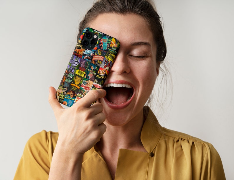 Puede incluir: Una mujer se r&iacute;e mientras sostiene una funda negra para iPhone con un collage de carteles de pel&iacute;culas de terror vintage. Los carteles presentan t&iacute;tulos como "Frankenstein", "Dr&aacute;cula", "La Criatura de la Laguna Negra" y "El Hombre Lobo".