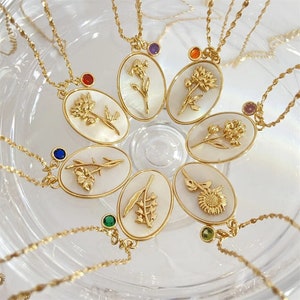 Könnte beinhalten: Sieben goldene Halsketten mit weißen Anhängern, die verschiedene Blumenmotive zeigen. Jeder Anhänger ist mit einem kleinen Edelstein verziert.