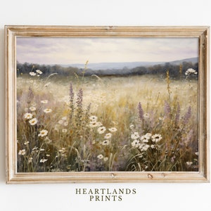 May include: A framed painting of a field of wildflowers, including daisies and purple wildflowers, with a distant view of a forest and hills in the background. The painting is in a light wood frame.
