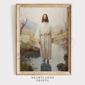 May include: A painting of Jesus Christ standing in a body of water. He is wearing a white robe and has long brown hair and a beard. The water is clear and reflects the sky and trees. The painting is framed in a light wood frame.