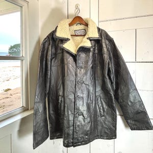 May include: A dark brown patchwork leather jacket featuring a cream-colored faux shearling collar and lining. The jacket has a button-front closure with four visible buttons and a Cellini brand label sewn inside the collar area.