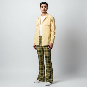 May include: A person wearing a light yellow button-up shirt with two chest pockets and plaid pants in green, yellow, and black. The outfit includes a white t-shirt and white sneakers. The pants have a flared leg design.