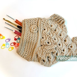 May include: A crocheted fish-shaped bag in beige with a textured pattern. The bag is filled with knitting needles and stitch markers.