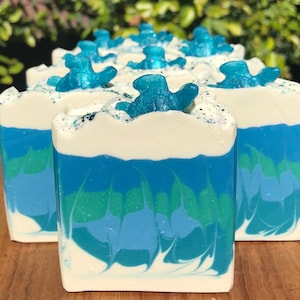 May include: A row of handmade soap bars with a blue, green, and white swirl design. Each bar is topped with a blue, glittery turtle figurine.