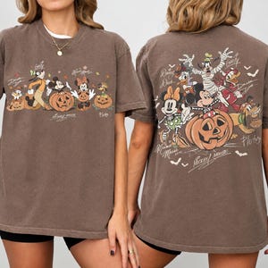 May include: Brown t-shirt featuring a Halloween-themed design with Disney characters, including Mickey Mouse, Minnie Mouse, and Goofy, with pumpkins. The front and back of the shirt display the characters and the words "Mickey Mouse".