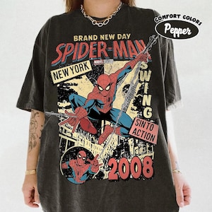May include: Charcoal grey t-shirt with a Spider-Man graphic. The design includes the words "Brand New Day," "Spider-Man," "New York," and "2008." The superhero is shown in action, swinging. The shirt is from Comfort Colors.