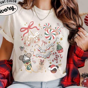 May include: Ivory Comfort Colors t-shirt featuring a festive Christmas design. The shirt showcases various holiday-themed graphics, including candy canes, gingerbread characters, and the phrase "Tis the Season."