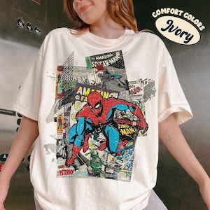 Pode incluir: Camiseta cor marfim com um gr&aacute;fico de quadrinhos do Homem-Aranha. O design inclui as palavras "AMAZING SPIDER-MAN" e "ZING MAN". Parte da cole&ccedil;&atilde;o "COMFORT COLORS".