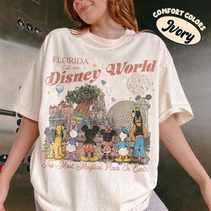 May include: Ivory t-shirt with a Disney World graphic. The design includes Disney characters, the text "FLORIDA Disney World" and "The Most Magical Place On Earth". The shirt is a comfort fit.