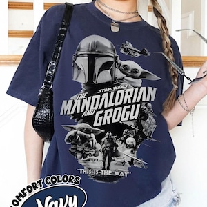 Op de afbeelding: Marineblauwe t-shirt met een grafisch ontwerp uit de Star Wars-serie, "The Mandalorian and Grogu". Het ontwerp bevat afbeeldingen van The Mandalorian, Grogu en een ruimteschip, met de zin "This is the Way."