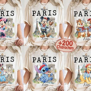 K&ouml;nnte beinhalten: Cremefarbene T-Shirts mit dem Wort "PARIS" in Schwarz, die Disney-Figuren wie Minnie Maus, Micky Maus, Chip und Chap, Goofy, Stitch und Pluto zeigen. Jedes Design enth&auml;lt den Eiffelturm und den Arc de Triomphe.