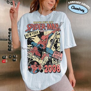 May include: Pale blue t-shirt with a Spider-Man graphic in a vintage style. The design includes the words "BRAND NEW DAY", "SPIDER-MAN", "NEW YORK", "SWING", "SIN TO ACTION", and "2008". The shirt has a distressed, retro aesthetic.