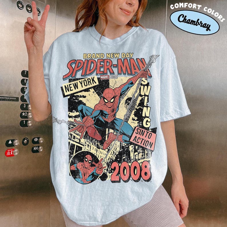 May include: Pale blue t-shirt with a Spider-Man graphic in a vintage style. The design includes the words "BRAND NEW DAY", "SPIDER-MAN", "NEW YORK", "SWING", "SIN TO ACTION", and "2008". The shirt has a distressed, retro aesthetic.