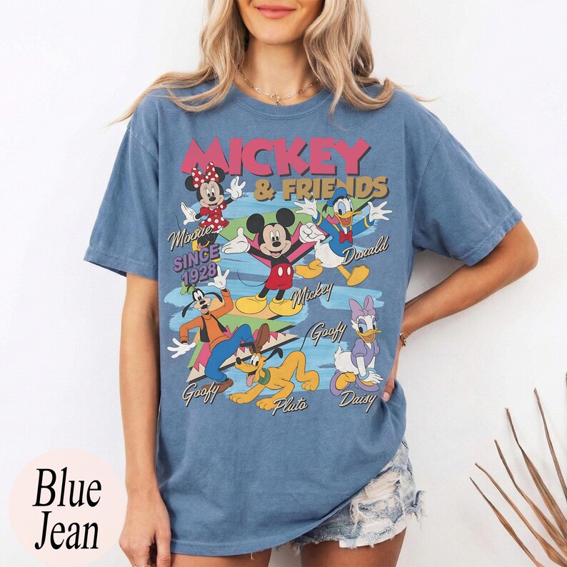Peut inclure: T-shirt bleu jean avec un motif de Mickey Mouse et ses amis. Le motif comprend Minnie Mouse, Donald Duck, Dingo, Pluto et Daisy Duck. Le texte "Mickey & Friends" et "Since 1928" est &eacute;galement affich&eacute;.
