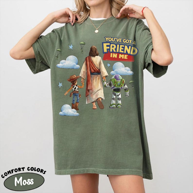 May include: Moss green t-shirt featuring the text "YOU'VE GOT A FRIEND IN ME" above an illustration of Jesus, Woody, and Buzz Lightyear. The shirt is a Comfort Colors brand.