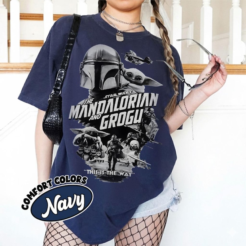 Op de afbeelding: Marineblauwe t-shirt met een grafisch ontwerp uit de Star Wars-serie, "The Mandalorian and Grogu". Het ontwerp bevat afbeeldingen van The Mandalorian, Grogu en een ruimteschip, met de zin "This is the Way."