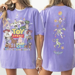 Op de afbeelding: Een lichtpaars t-shirt met Toy Story-personages op de voorkant, waaronder Woody, Buzz Lightyear en Jessie, met de tekst Toy Story en You've Got a Friend in Me. De achterkant toont een verticale rangschikking van personage-iconen.