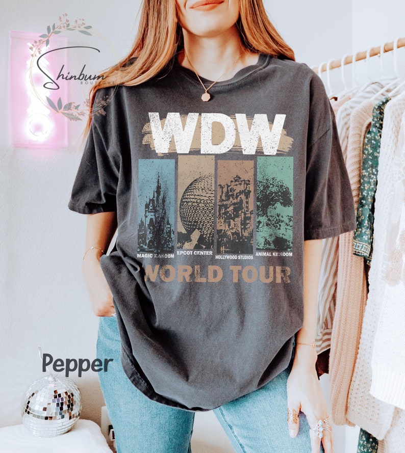 May include: A dark grey t-shirt with a vintage-style graphic of the Walt Disney World logo and the text "World Tour". The graphic features images of the Magic Kingdom, Epcot Center, Hollywood Studios, and Animal Kingdom.