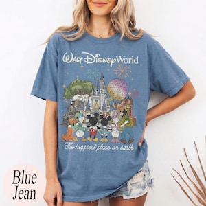 Puede incluir: Camiseta azul vaquera con un gr&aacute;fico de Walt Disney World. El dise&ntilde;o presenta el castillo de Disney World, personajes, fuegos artificiales y el texto "The happiest place on earth". La camiseta tambi&eacute;n tiene el texto "Walt Disney World" en la parte superior.