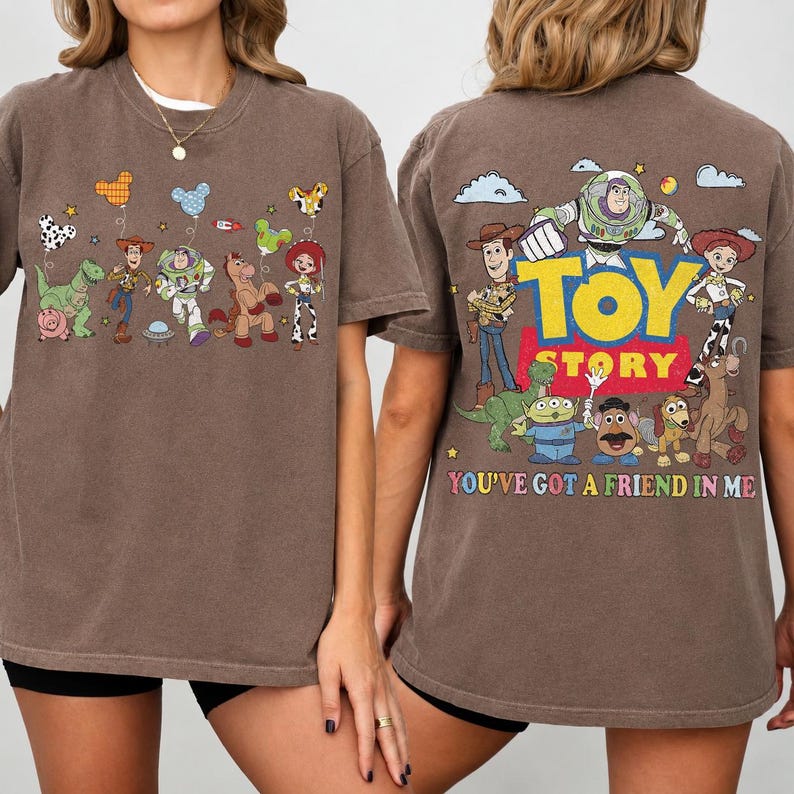 May include: A brown t-shirt featuring Toy Story characters. The front displays small illustrations of Woody, Buzz Lightyear, Rex, and Jessie with balloons. The back shows a large Toy Story logo with the characters and the text You've Got A Friend In Me.