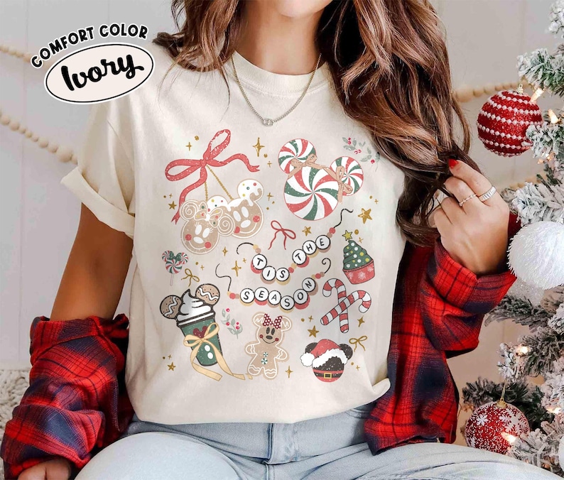 May include: Ivory Comfort Colors t-shirt featuring a festive Christmas design. The shirt showcases various holiday-themed graphics, including candy canes, gingerbread characters, and the phrase "Tis the Season."