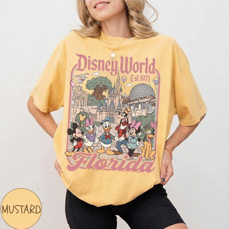 May include: Mustard yellow t-shirt featuring a Disney World graphic with Mickey Mouse, Minnie Mouse, Donald Duck, Daisy Duck, Goofy, and Pluto. The graphic includes the text "Disney World Est. 1971 Florida" in a vintage style.