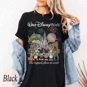Puede incluir: Camiseta negra con un gr&aacute;fico colorido de Walt Disney World, que incluye monumentos emblem&aacute;ticos, fuegos artificiales y personajes de Disney. El texto "Walt Disney World" y "The happiest place on earth" est&aacute;n impresos.