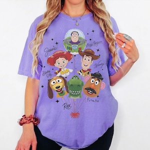 Puede incluir: Una camiseta de color lila con un dise&ntilde;o de personajes de Toy Story. El dise&ntilde;o incluye a Buzz Lightyear, Woody, Jessie, Slinky Dog, Rex y Mr. Potato. Los nombres de los personajes est&aacute;n escritos en una fuente caprichosa, con estrellas.