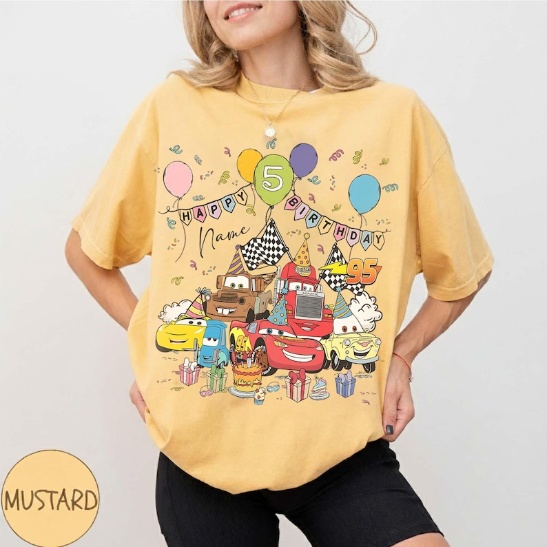 K&ouml;nnte beinhalten: Senfgelbes T-Shirt mit einem farbenfrohen Cartoon-Auto-Geburtstagsdesign. Die Grafik zeigt Ballons, einen Kuchen und die Worte "HAPPY BIRTHDAY" und "Name". Die Zahl "5" ist ein zentrales Element des Designs.