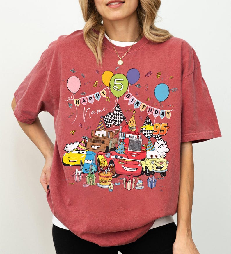 K&ouml;nnte beinhalten: R&ouml;tliches T-Shirt mit einer bunten Grafik von Cartoon-Autos, die einen Geburtstag feiern. Das Design umfasst Luftballons, die Zahl 5 und die W&ouml;rter "Happy Birthday" und "Name". Die Zahl 95 ist ebenfalls sichtbar.