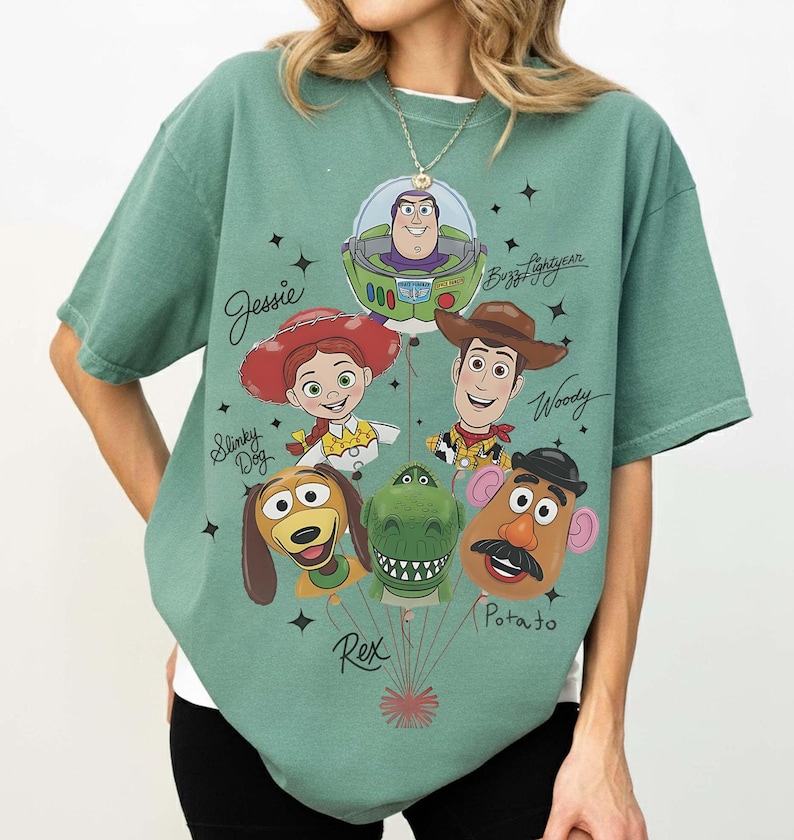 Puede incluir: Camiseta verde salvia con un gr&aacute;fico de personajes de Toy Story como globos. El dise&ntilde;o incluye a Buzz Lightyear, Woody, Jessie, Slinky Dog, Rex y Mr. Potato. Los nombres de los personajes est&aacute;n escritos encima.