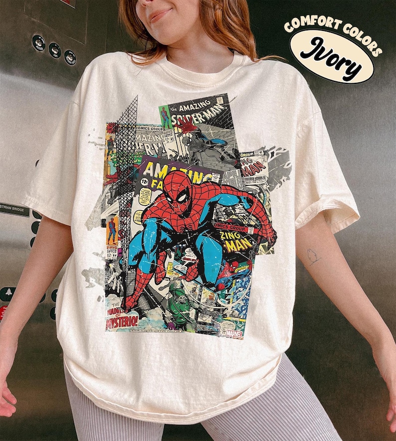 Pode incluir: Camiseta cor marfim com um gr&aacute;fico de quadrinhos do Homem-Aranha. O design inclui as palavras "AMAZING SPIDER-MAN" e "ZING MAN". Parte da cole&ccedil;&atilde;o "COMFORT COLORS".