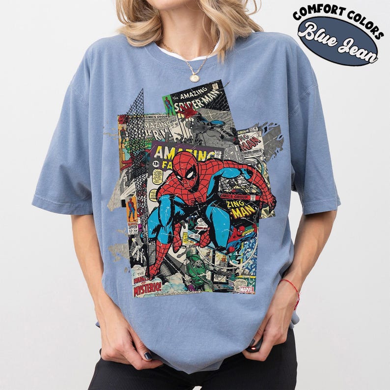 Pode incluir: T-shirt azul jeans com um gr&aacute;fico do Homem-Aranha em a&ccedil;&atilde;o, em um collage de capas de quadrinhos. A camisa inclui o texto "COMFORT COLORS" e "Blue Jean".