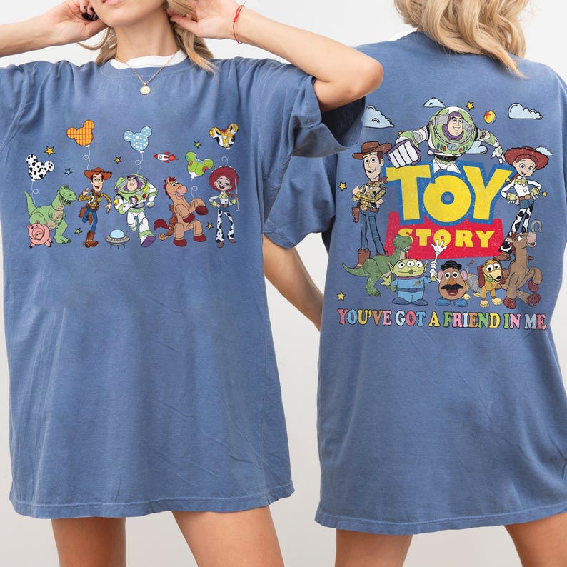 May include: A blue t-shirt featuring Toy Story characters. The front displays Woody, Buzz Lightyear, Rex, Hamm, Bullseye, and Jessie with balloons. The back shows the Toy Story logo and characters with the text YOU'VE GOT A FRIEND IN ME.