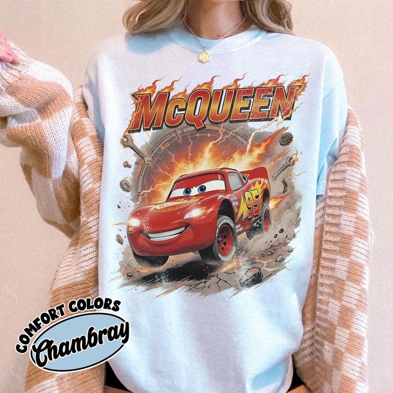 Może przedstawiać: Jasnoniebieska bluza z grafiką Zygzaka McQueena z filmu Auta. Projekt zawiera napis "McQueen" w płomieniach, numer "95" oraz słowa "Comfort Colors Chambray".