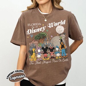 May include: Brown t-shirt with a retro Disney World graphic. The design includes Mickey and Minnie Mouse, and the text "The Most Magical Place On Earth". The shirt is a comfort colors style in the colour Espresso.