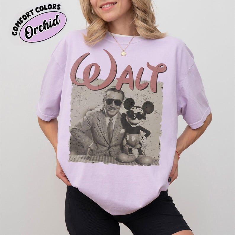 May include: A light purple t-shirt featuring a vintage graphic of Walt Disney with Mickey Mouse. The word "Walt" is printed in a retro style above the image. The shirt also has the text "Comfort Colors Orchid" in a circle.