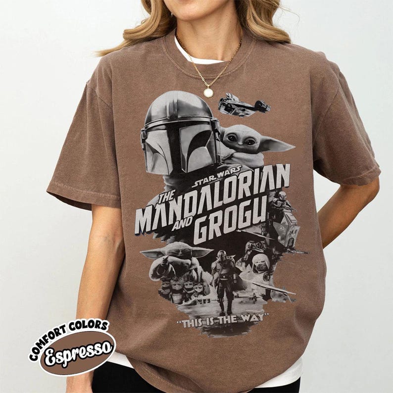 Op de afbeelding: Espresso-kleurig T-shirt met een afbeelding van Star Wars: The Mandalorian and Grogu. Het ontwerp bevat de helm van de Mandalorian, Grogu en de tekst "THE MANDALORIAN AND GROGU". De zin "THIS IS THE WAY" staat ook op het shirt.