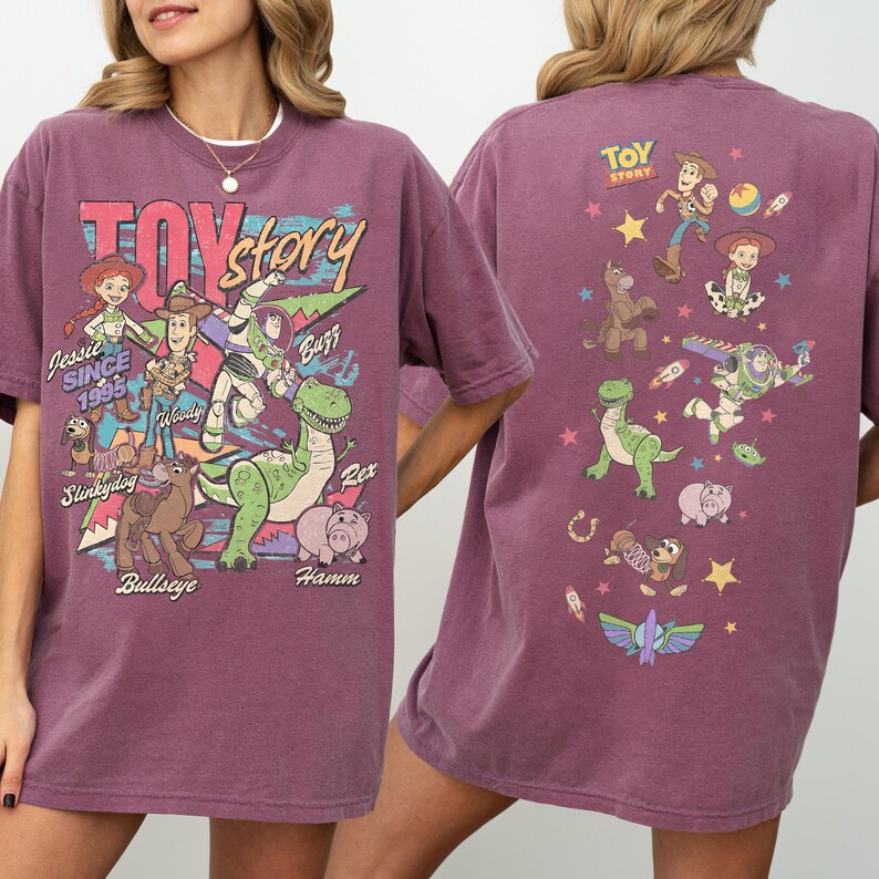 May include: A maroon-colored t-shirt featuring the words "Toy Story" in a retro font, along with illustrations of characters like Woody, Buzz, and Rex. The back of the shirt displays additional character graphics and the "Toy Story" logo.