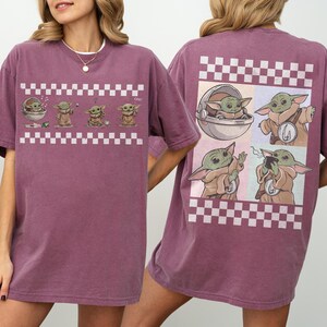 May include: A maroon t-shirt featuring a cartoon character design. The front of the shirt displays a series of the character in a checkered pattern. The back of the shirt has a larger design of the character in a checkered pattern.