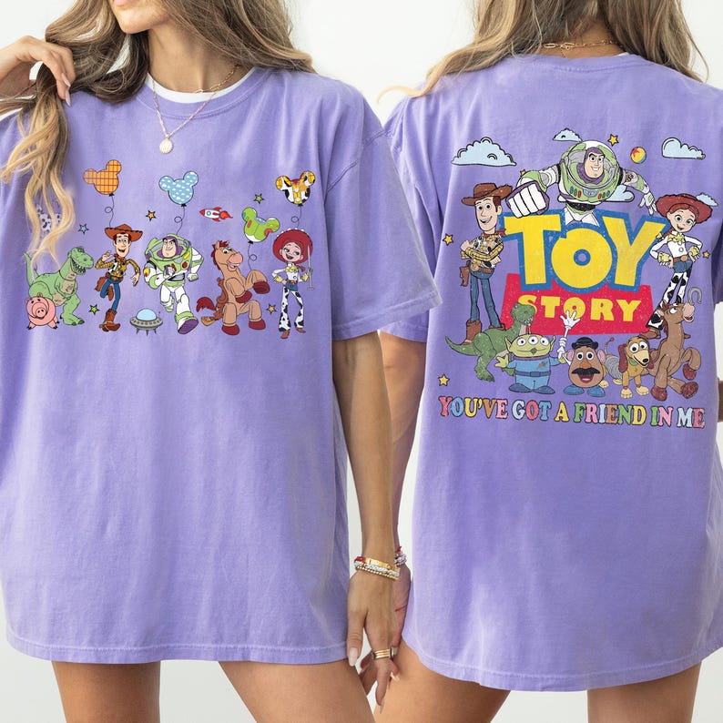 May include: A light purple t-shirt featuring Toy Story characters. The front displays Woody, Buzz Lightyear, Rex, Bullseye, and Jessie with balloons. The back shows the Toy Story logo, the characters, and the text You've Got A Friend In Me.
