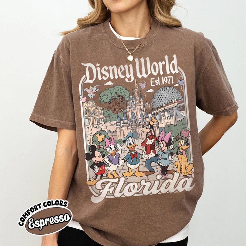 May include: Brown t-shirt featuring a Disney World graphic with Mickey Mouse, Donald Duck, and other characters. The design includes the text "Disney World Est. 1971 Florida". The shirt is labeled "Comfort Colors Espresso".