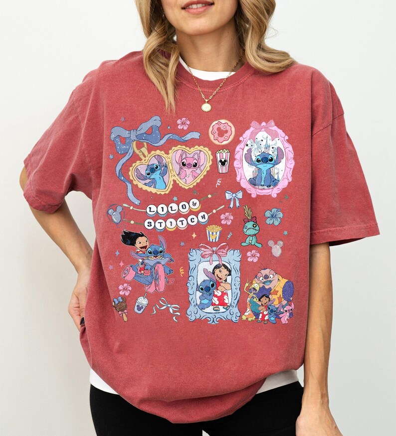 May include: A maroon t-shirt featuring a colorful graphic design with the text "LOLO STITCH". The design includes cartoon characters in frames, bows, and floral elements. The shirt is made of a soft material.