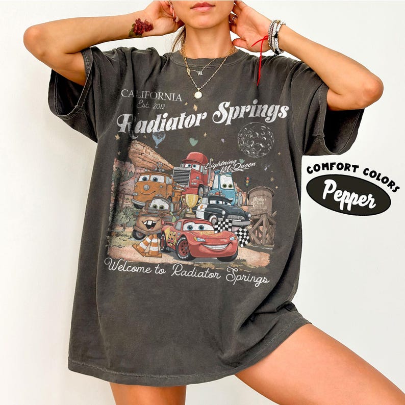 以下が含まれることがあります： 映画「カーズ」のキャラクターのグラフィックがプリントされた濃いグレーのTシャツ。「California Est. 2012 Radiator Springs Welcome to Radiator Springs」の文字入り。シャツには「Comfort Colors Pepper」と記載。