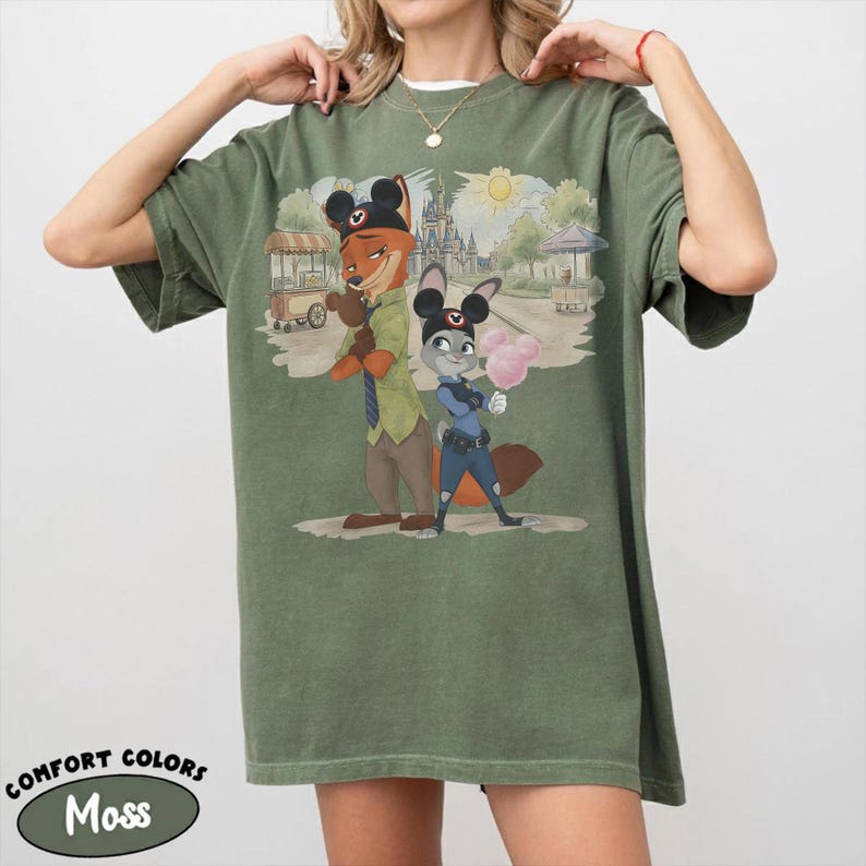 Puede incluir: Camiseta Comfort Colors verde musgo con una ilustraci&oacute;n de dibujos animados de Nick Wilde y Judy Hopps de Zootopia, con orejas de Mickey Mouse. La imagen incluye un castillo, un sol y el texto "Comfort Colors Moss".
