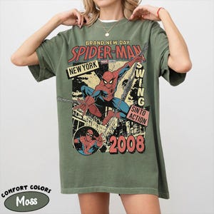 May include: Moss green t-shirt with a vintage Spider-Man graphic. The design includes the words "BRAND NEW DAY", "SPIDER-MAN", "NEW YORK", and "2008". The shirt is made of Comfort Colors material.