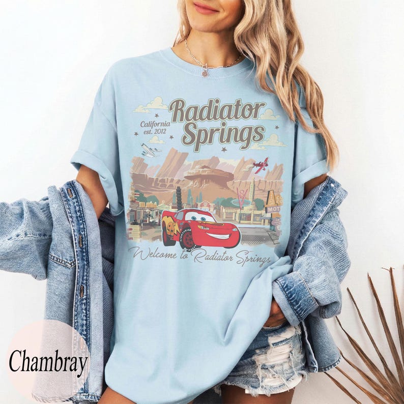 May include: Pale blue t-shirt with a graphic of Radiator Springs, including the text "Radiator Springs California est. 2012" and "Welcome to Radiator Springs". The graphic features a red race car.