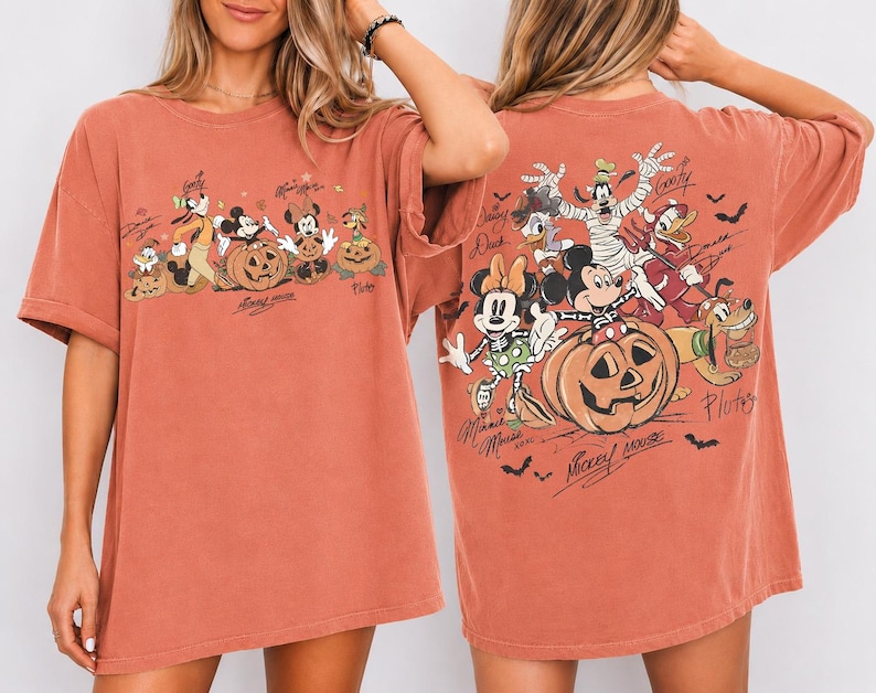 May include: Rust-colored oversized t-shirt featuring a Halloween-themed graphic of Disney characters, including Mickey Mouse, Minnie Mouse, and Goofy, with pumpkins. The back of the shirt also has a similar design. The text "Mickey Mouse" is visible.