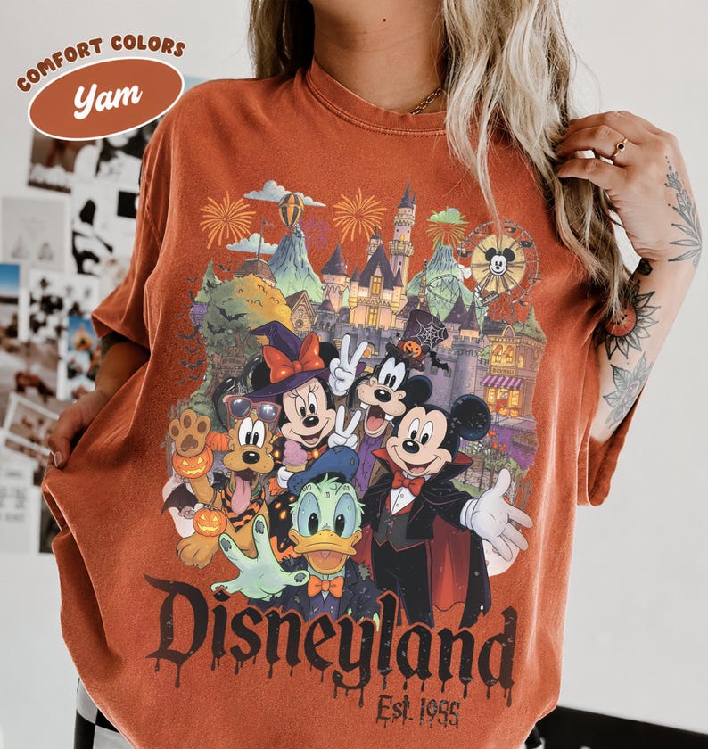 May include: A yam-colored t-shirt featuring a graphic of Disney characters in Halloween costumes, including Mickey, Minnie, Goofy, Donald, and Pluto in front of a castle. The text reads Disneyland Est. 1955 and Comfort Colors Yam.